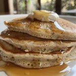 Close-up of fluffy vegan pancakes stacked high, with a drizzle of syrup.