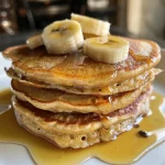 Close-up view of fluffy banana pancakes stacked, with a banana slice on top.
