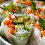 A close-up side view of fresh avocado spring rolls with vibrant vegetables and peanut ginger sauce.