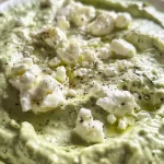Close-up of creamy Green Goddess Whipped Feta Dip in a bowl, topped with fresh herbs.