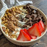 Close-up of a high-protein Greek yogurt bowl with diced strawberries, dark chocolate chunks, and walnuts.