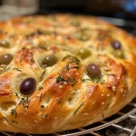 A close-up view of a Holiday Focaccia Wreath adorned with olives and rosemary.