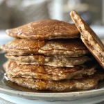 A close-up side view of golden-brown oatmeal protein pancakes stacked on a plate.