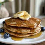 Close-up of fluffy Protein Oatmeal Blender Pancakes topped with fresh blueberries.