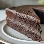 A side view close-up of a rich chocolate cake topped with glossy chocolate ganache.