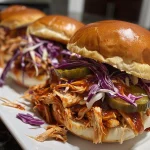 Close-up view of juicy BBQ pulled chicken sliders with coleslaw and pickles on a wooden surface.