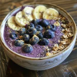 Close-up of a colorful smoothie bowl topped with blueberries, sliced bananas, and granola.