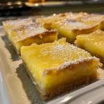 A close-up view of freshly baked lemon bars on a white plate, showcasing their golden crust and zesty topping.