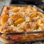 A close-up side view of a juicy Peach Dump Cake with a golden cake layer and visible peach slices.