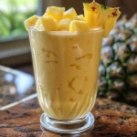 Close-up of a vibrant pineapple coconut smoothie in a clear glass with tropical garnishes.