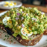 Close-up of a vibrant avocado egg salad toast, garnished with paprika.