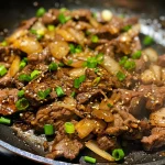 Close-up view of juicy Black Pepper Beef with garnished green onions.