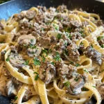 Close-up view of creamy beef and mushroom pasta with rich sauce and herbs.