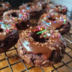 Close-up view of healthy chocolate protein donuts with a glossy chocolate drizzle and colorful sprinkles.