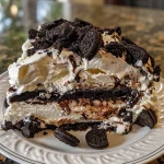 Side view of a decadent Ice Cream Sandwich Oreo Cake topped with whipped cream and drizzled with hot fudge.