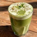 Close-up side view of a refreshing iced matcha latte with ice and a mint leaf on top.