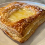 Close-up view of a golden-brown Lemon Cream Cheese Danish with a glossy lemon glaze.