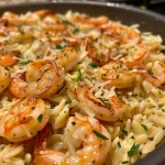 Close-up of a creamy One Pan Parmesan Orzo with plump shrimp, set against a bright background.