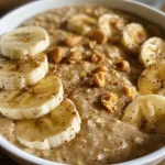 Close-up side view of a bowl filled with Peanut Butter Banana Protein Oats garnished with sliced bananas.