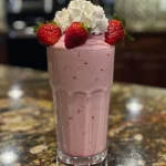 Close-up side view of a vibrant strawberry protein shake in a clear glass.