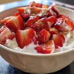 A close-up view of a bowl of creamy strawberry yogurt with fresh strawberry pieces.