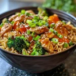 A close-up side view of a bowl filled with Teriyaki chicken, noodles, and colorful vegetables.