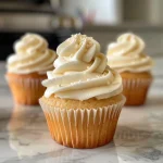 Close-up side view of a fluffy vanilla cupcake topped with creamy frosting.