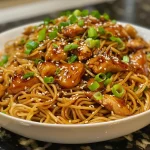 A close-up of chicken teriyaki noodles garnished with vegetables.