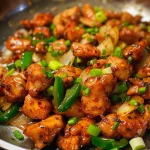 Close-up view of juicy Chilli Chicken served with green peppers and onions.
