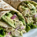 A close-up view of a creamy avocado chicken salad wrap filled with shredded chicken, avocado, and diced vegetables.