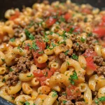 Close-up view of creamy beef and pasta skillet with melting cheese and fresh parsley.