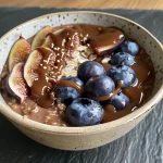 Close-up view of creamy chocolate oatmeal topped with fresh blueberries and figs.