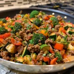 Close-up view of a colorful ground beef veggie skillet on a wooden table.