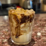 Close-up side view of a frosty iced vanilla latte in a clear glass.