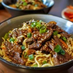 Close-up view of sticky beef noodles with colorful vegetables.