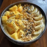 A vibrant tropical smoothie bowl topped with mango chunks, pineapple, and sliced banana.