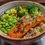 ['Close-up side view of a Baked Teriyaki Salmon Bowl with vibrant vegetables.', 'Juicy salmon fillet atop a bed of brown rice, garnished with broccoli and edamame.', 'Colorful Baked Teriyaki Salmon Bowl featuring sesame seeds and green onions.', 'Delicious meal showcasing salmon, rice, and fresh veggies in an appealing arrangement.']