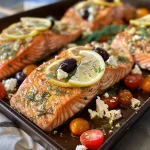 ['Close-up of a juicy baked salmon fillet topped with cherry tomatoes and garnished with lemon slices and olives.', 'Side view of flavorful Easy Baked Greek Salmon with vibrant cherry tomatoes and herbs, served on a plate.', 'Tender salmon fillets drizzled with olive oil, sprinkled with fresh dill and garnished with feta cheese and lemon.', 'Succulent salmon served with colorful side garnishes of Kalamata olives, lemon slices, and cherry tomatoes.']