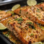 ['Close-up of a deliciously glazed Honey Lime Garlic Butter Baked Salmon fillet topped with fresh lime slices and cilantro.', 'Juicy salmon fillet with a golden honey-lime glaze, garnished with lime slices and cilantro, served on a white plate.', 'Side view of baked salmon drizzled with honey-lime garlic butter, showing its tender texture and vibrant garnishes.', 'A succulent piece of salmon fillet glazed with honey and lime, garnished with fresh lime and cilantro on a light background.']