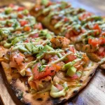 ['Close-up view of a juicy salmon flatbread topped with avocado mayonnaise and pico de gallo.', 'Side view of a delicious salmon flatbread garnished with pickles and celery on a toasted flatbread.', 'Detailed close-up of an appetizing flatbread featuring salmon, cheese, and fresh toppings.', 'Vibrant presentation of a salmon flatbread, highlighting its colorful ingredients and textures.']