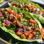 ['A close-up view of turkey taco lettuce wraps filled with colorful ingredients.', 'Juicy turkey taco lettuce wraps with diced avocado and cherry tomatoes on a wooden plate.', 'A side perspective of fresh lettuce wraps loaded with ground turkey and topped with crema.', 'Chewy turkey taco lettuce wraps featuring red onion and cilantro, garnished with lime slices.']