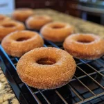 ['Close-up view of Baked Apple Cider Donuts topped with cinnamon sugar.', 'Side view of fluffy Baked Apple Cider Donuts on a white plate.', 'Juicy Baked Apple Cider Donuts arranged neatly with a rustic backdrop.', 'Freshly baked Baked Apple Cider Donuts sprinkled with spices.']