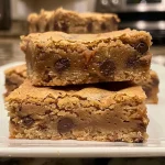 ['Close-up side view of a golden-brown chocolate chip blondie with gooey chocolate chunks.', 'A delicious slice of brown butter chocolate chip blondie showcasing its rich texture and melted chocolate.', 'Side view of a decadent blondie featuring dark chocolate chips in a warm, soft baked dessert.', 'Close-up image of a gooey chocolate chip blondie, highlighting the brown butter crust and chocolate pieces.']