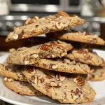 ['A close-up side view of golden-brown butter pecan cookies with chocolate chunks and pecans on top.', 'Deliciously baked brown butter pecan cookies with a rich, golden hue and chocolate pieces visible.', 'Side view of soft, chewy brown butter pecan cookies sprinkled with chopped pecans and chocolate chunks.', 'A detailed look at warm brown butter pecan cookies showcasing their texture and toppings.']