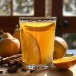 ['A close-up view of a glass of pear cider with a slice of orange and cinnamon sticks.', 'Juicy pear cider in a glass, garnished with orange slices and spices.', 'Side view of a refreshing pear cider, highlighting its golden color and garnishes.', 'Close-up shot of a frothy pear cider drink with decorative fruit and spice elements.']