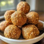 ['Close-up view of golden-brown pumpkin protein balls on a wooden surface.', 'Side view of pumpkin protein balls with a soft texture and pumpkin seeds sprinkled on top.', 'Array of round, orange-hued protein balls displayed on a rustic table.', 'Juicy pumpkin protein balls arranged neatly, highlighting their chewy consistency.']