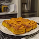 ['Close-up view of a sliced pumpkin roll showcasing a creamy filling.', 'Side view of a pumpkin roll dessert with a rich cream cheese filling.', 'Juicy pumpkin roll on a plate, highlighting its soft texture and filling.', 'Delicious pumpkin roll with visible layers of cake and cream cheese frosting.']