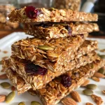 ['Close-up view of pumpkin spice granola bars with a golden-brown hue and visible cranberries and seeds.', 'Side view of chewy pumpkin spice granola bars showcasing oats and a sprinkle of pepitas.', 'Detailed shot of homemade pumpkin spice granola bars, highlighting textures and ingredients like cranberries and oats.', 'Close-up image of pumpkin spice granola bars, featuring a rustic, wholesome appearance and colorful ingredients.']