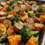 ['Close-up view of juicy sausage and sweet potatoes with broccoli on a sheet pan.', 'A side perspective of a sheet pan filled with roasted chicken sausage, sweet potatoes, and garlic sauce.', 'Colorful dish of sliced sausage and cubed sweet potatoes garnished with parsley and garlic.', 'A vibrant arrangement of cooked sausage, sweet potatoes, and broccoli drizzled with honey garlic sauce.']