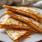 Close-up of two Jack-o-lantern shaped cheese quesadillas filled with melted cheese.